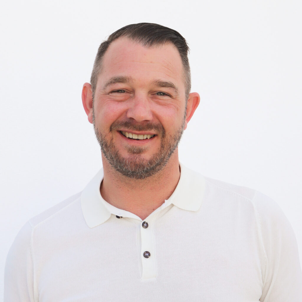 A person smiling, wearing a white collared shirt against a plain background.